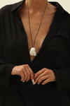 Person wearing a sea snail pendant on a black cord and a black outfit with a white background