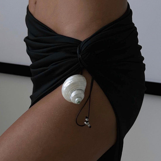 Person wearing a black sarong with a white shell accessory on a plain background