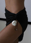 Person wearing a black sarong with a white shell accessory on a plain background