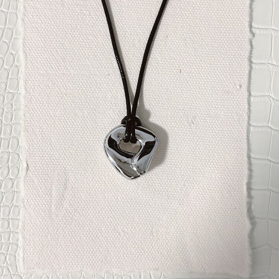 silver knot circle shaped pendant on a black cord against a textured white background