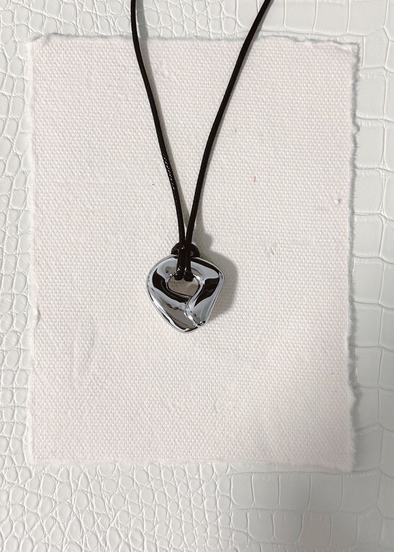 silver knot circle shaped pendant on a black cord against a textured white background