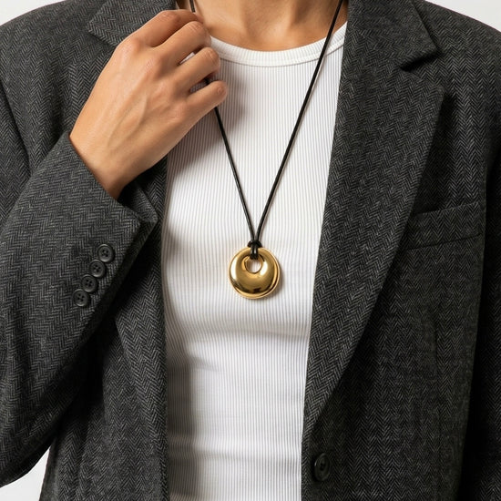 Person wearing a gold circle pendant cord 
necklace with a plain background