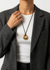 Person wearing a gold circle pendant cord 
necklace with a plain background