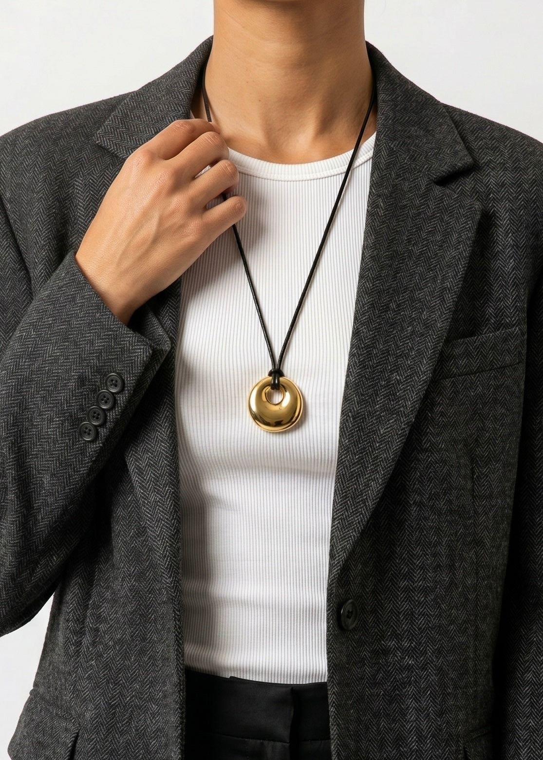 Person wearing a gold circle pendant cord 
necklace with a plain background