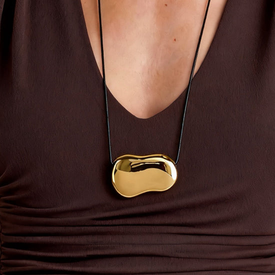 Gold necklace with a unique pendant on a brown garment