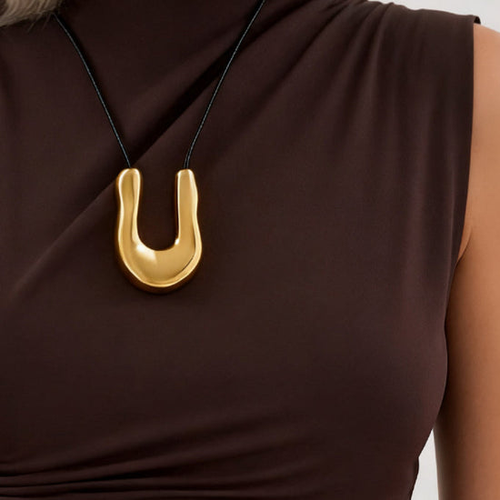 Gold necklace with a u shape pendant on a brown top against a neutral background