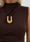 Gold necklace with a u shape pendant on a brown top against a neutral background