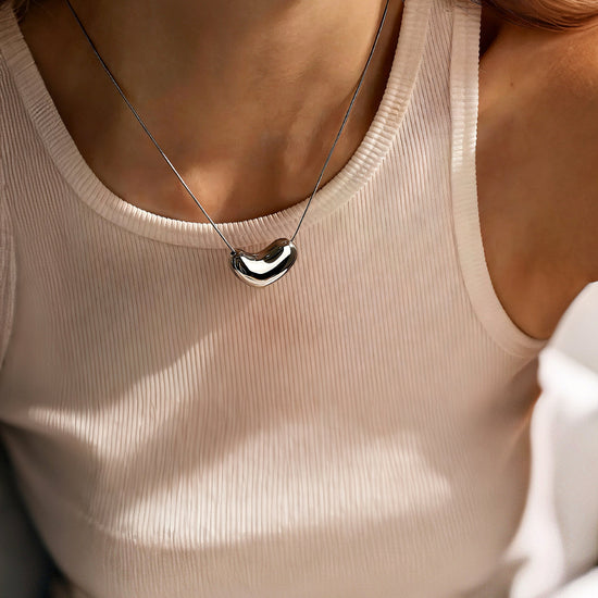 Person wearing a beige tank top with a necklace featuring a silver heart pendant.