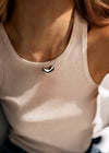 Person wearing a beige tank top with a necklace featuring a silver heart pendant.