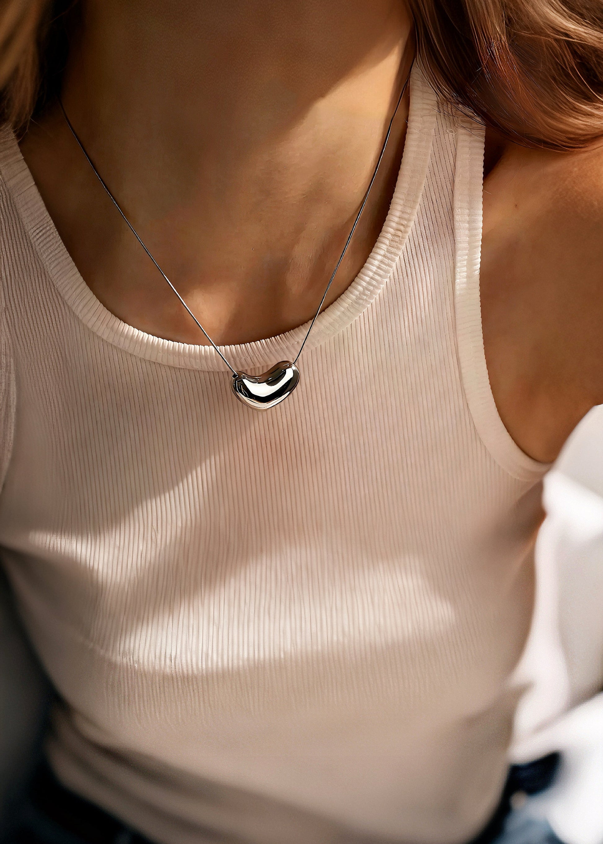 Person wearing a beige tank top with a necklace featuring a silver heart pendant.