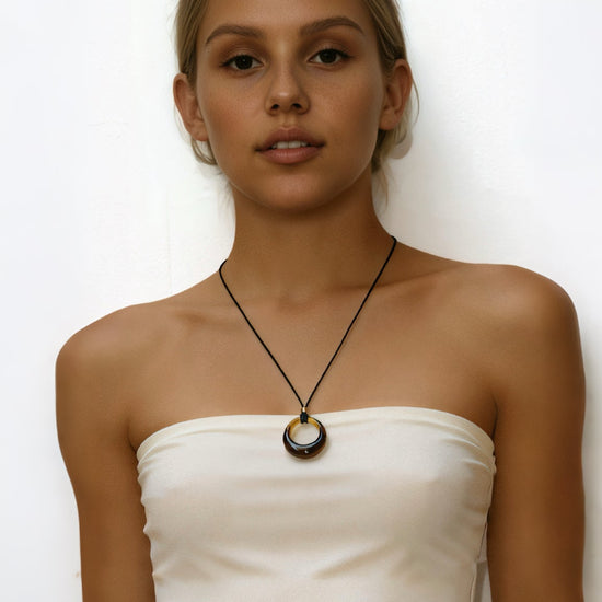 Woman wearing a white strapless top and black skirt with a amber circle pendant cord necklace on a white background