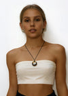 Woman wearing a white strapless top and black skirt with a amber circle pendant cord necklace on a white background