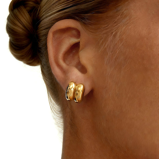 Close-up of a person wearing gold dainty hoop shape stud earrings with a plain background