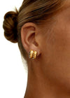 Close-up of a person wearing gold dainty hoop shape stud earrings with a plain background