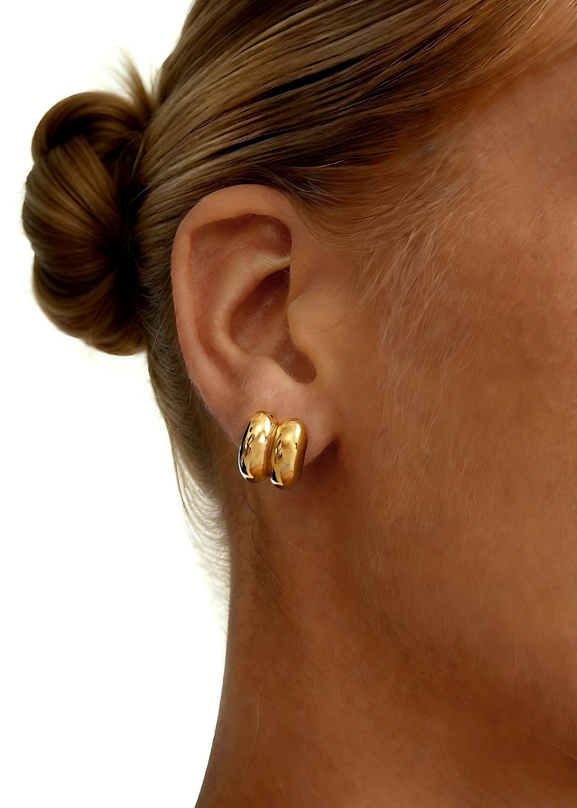 Close-up of a person wearing gold dainty hoop shape stud earrings with a plain background