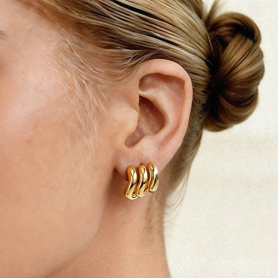 Gold hoop earrings worn by a person with a neutral background