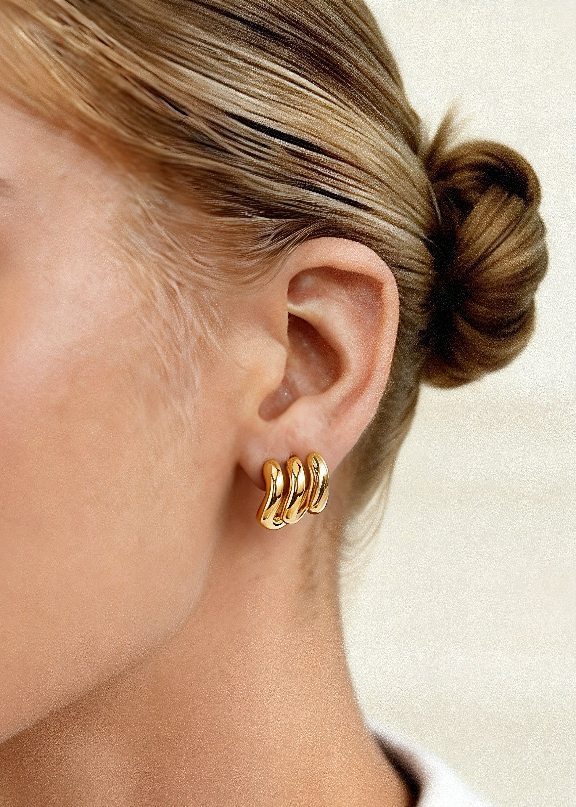 Gold hoop earrings worn by a person with a neutral background