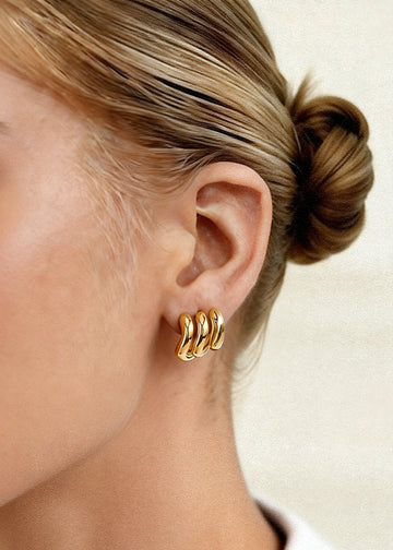 Gold hoop earrings worn by a person with a neutral background