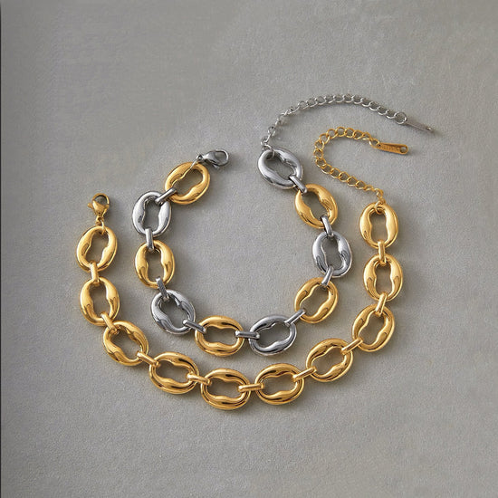 Two chain necklaces, one gold and one silver, on a gray background