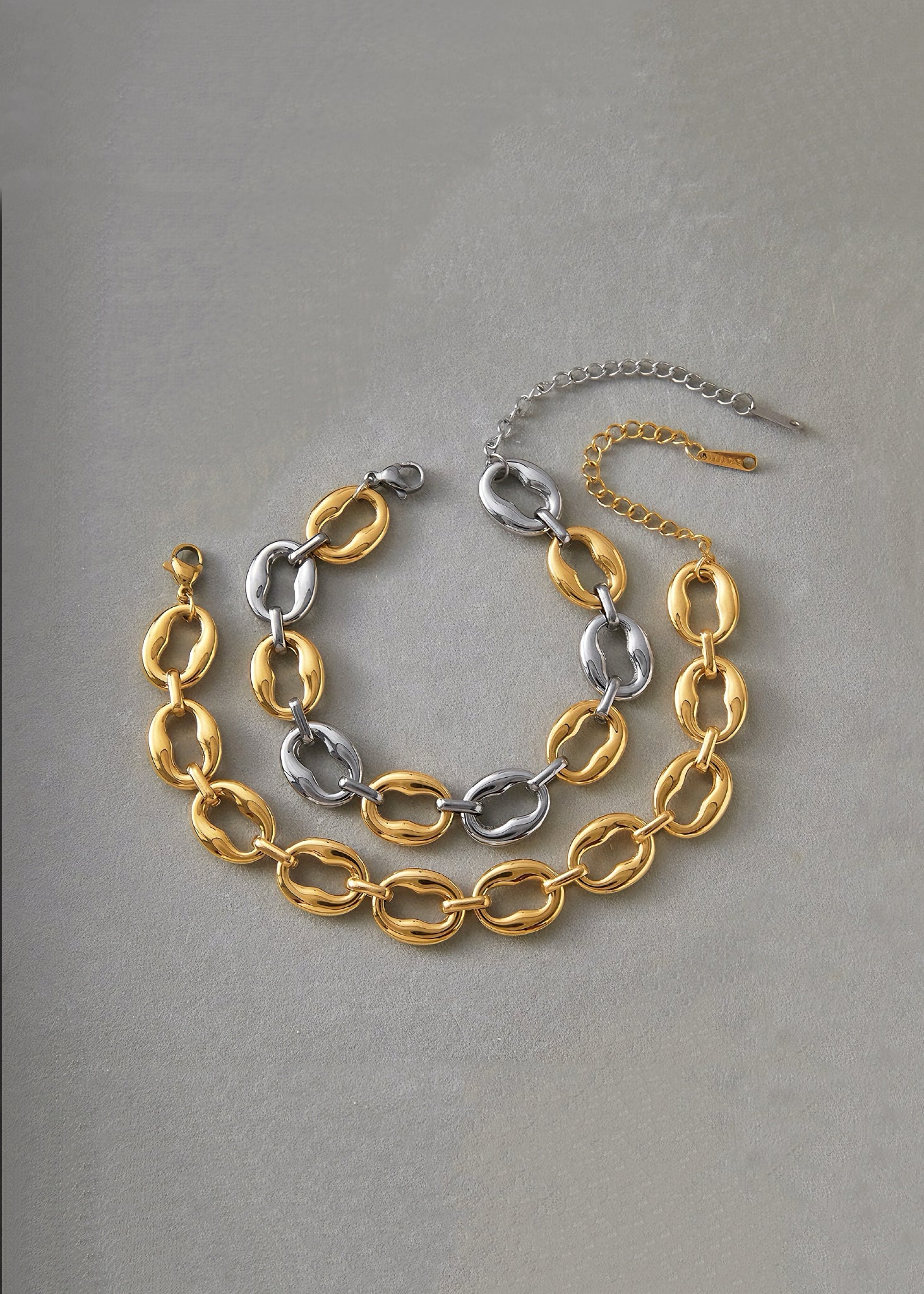 Two chain necklaces, one gold and one silver, on a gray background