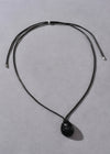 Black necklace with a oval pendant on a gray background
