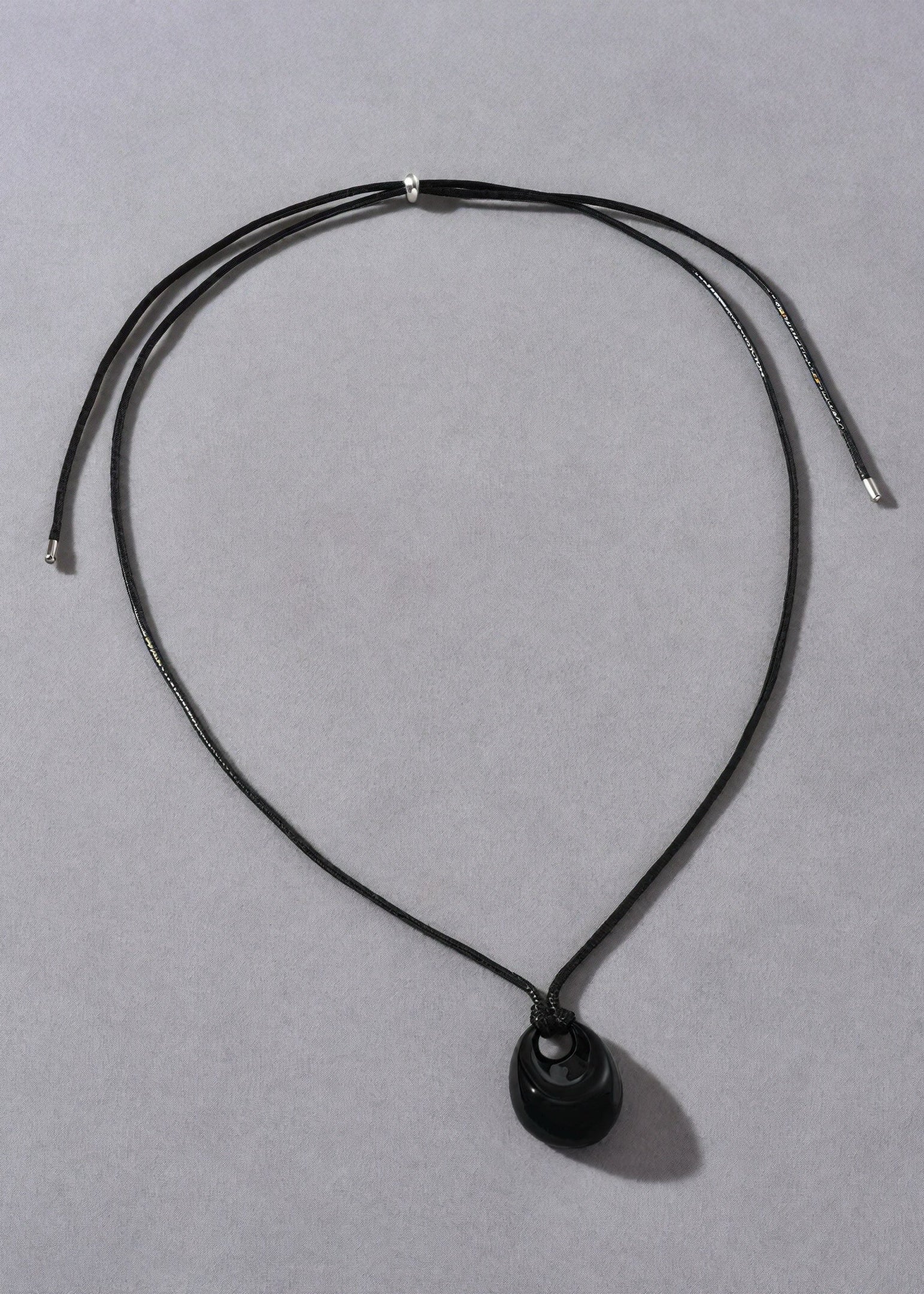 Black necklace with a oval pendant on a gray background