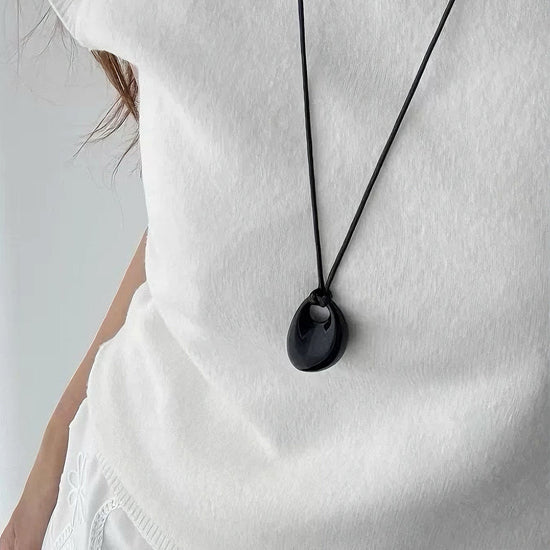 Person wearing a white top with a black pendant necklace on a plain background