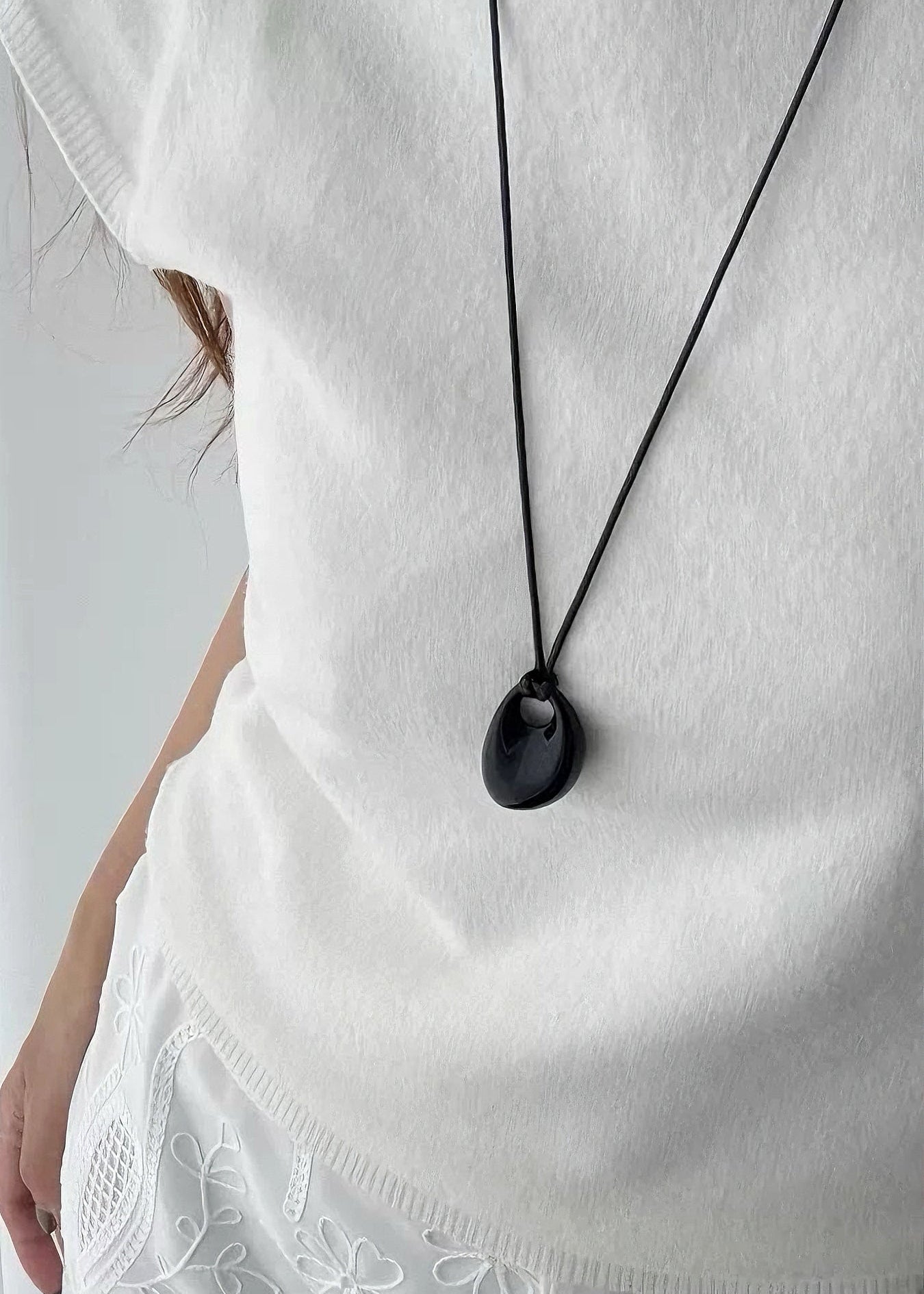 Person wearing a white top with a black pendant necklace on a plain background