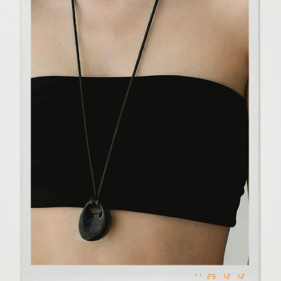 Black necklace with a pendant on a person wearing a black top.