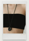 Black necklace with a pendant on a person wearing a black top.