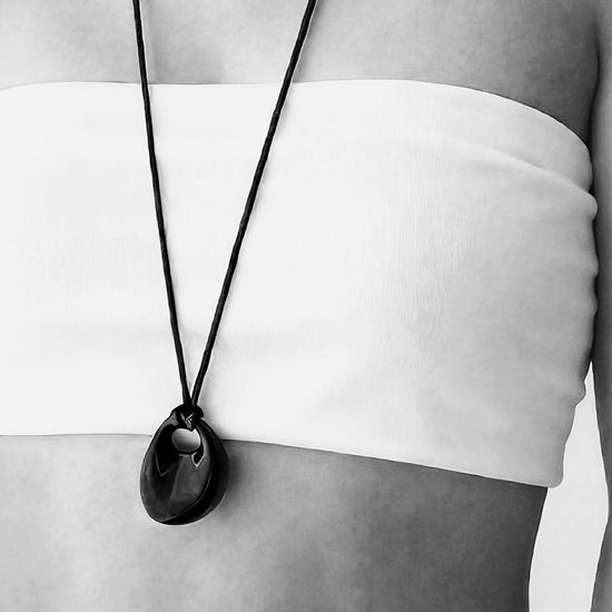 Person wearing a long necklace with a black pendant, black and white photo