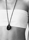 Person wearing a long necklace with a black pendant, black and white photo