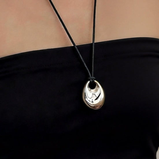 Black necklace with a pendant on a person wearing a black top.