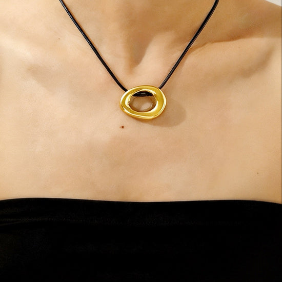 Gold necklace with a black cord worn by a person against a neutral background
