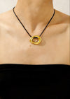 Gold necklace with a black cord worn by a person against a neutral background