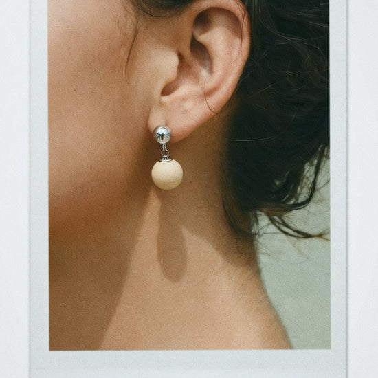 Close-up of an ear wearing a off-white ball stone drop earring with a soft focus background