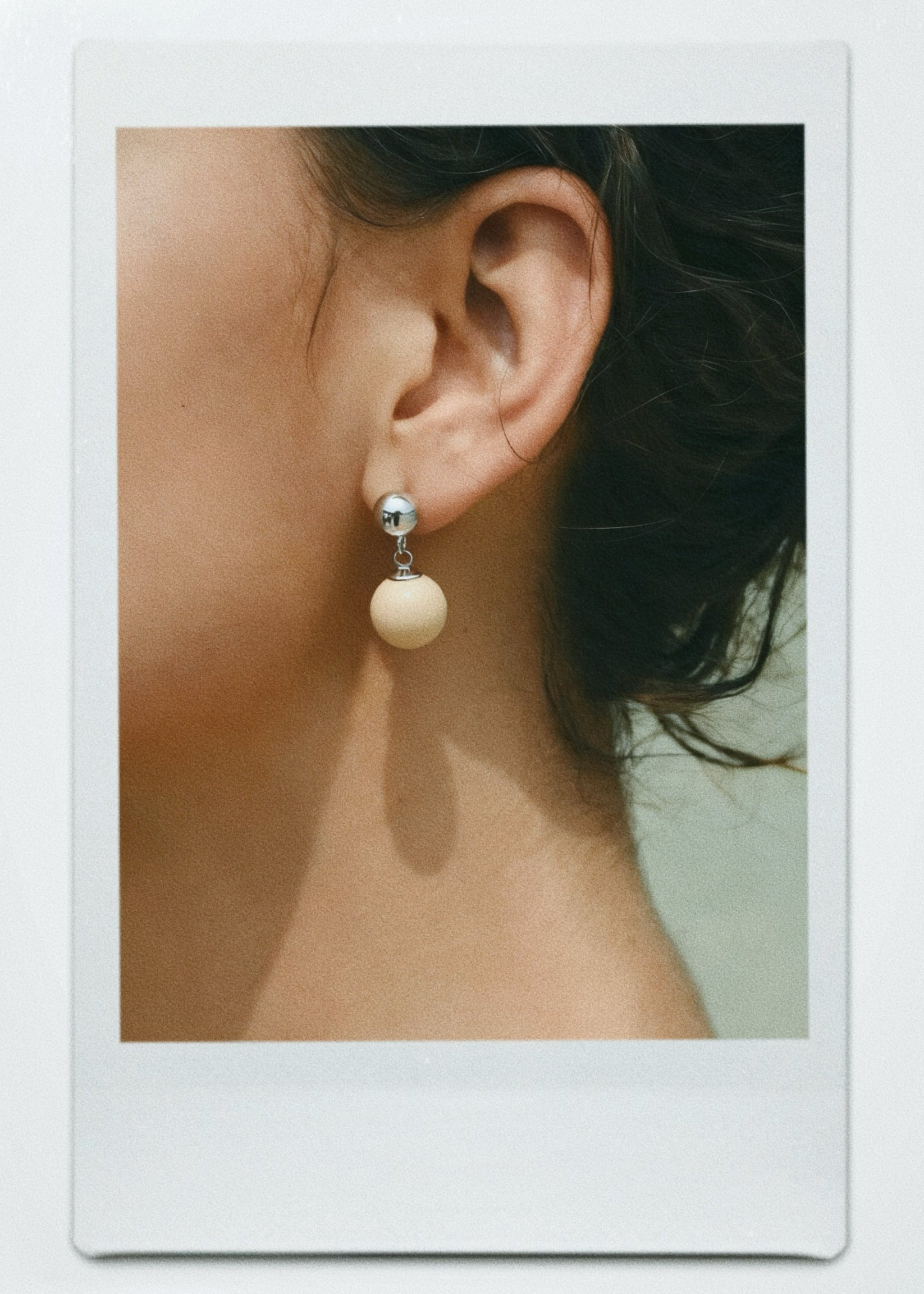 Close-up of an ear wearing a off-white ball stone drop earring with a soft focus background