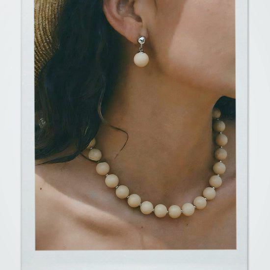 Close-up of a person wearing an off-white ball stone drop earring and necklace.