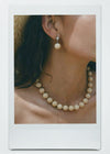 Close-up of a person wearing an off-white ball stone drop earring and necklace.