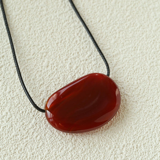 Red stone pendant on a black cord against a beige background