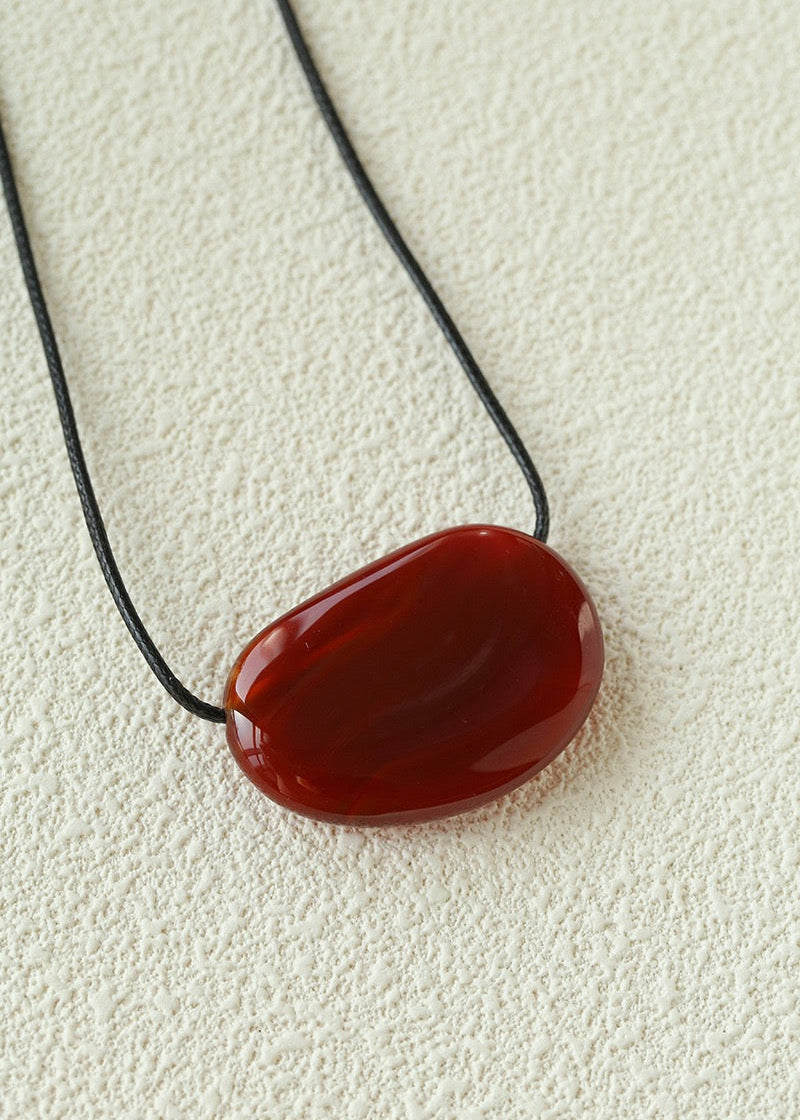 Red stone pendant on a black cord against a beige background