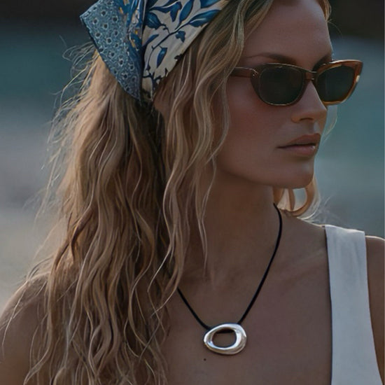 Woman wearing a headscarf, sunglasses and a silver circle pendant on a black cord with a blurred background