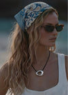 Woman wearing a headscarf, sunglasses and a silver circle pendant on a black cord with a blurred background