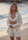 Woman wearing a black bead pendant on a black cord and a beige outfit standing on a beach