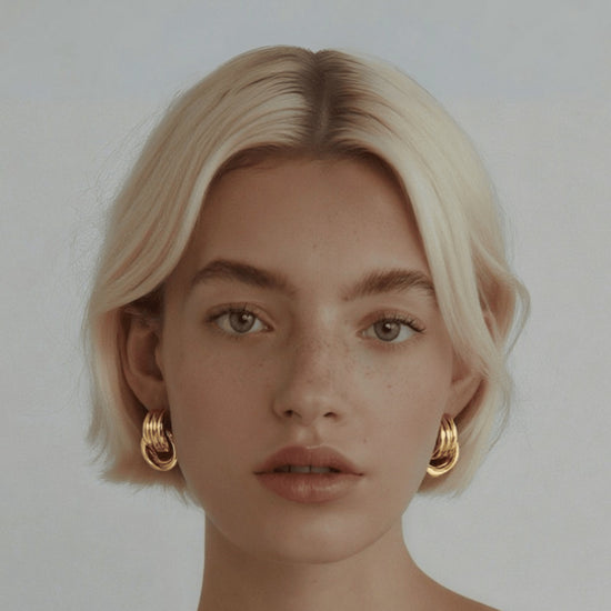 Woman wearing gold hoop earrings against a plain background