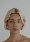 Woman wearing gold hoop earrings against a plain background