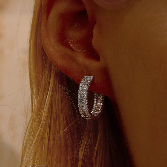 Close-up of an ear wearing a silver cubic zirconia hoop earring with blurred backgrounD