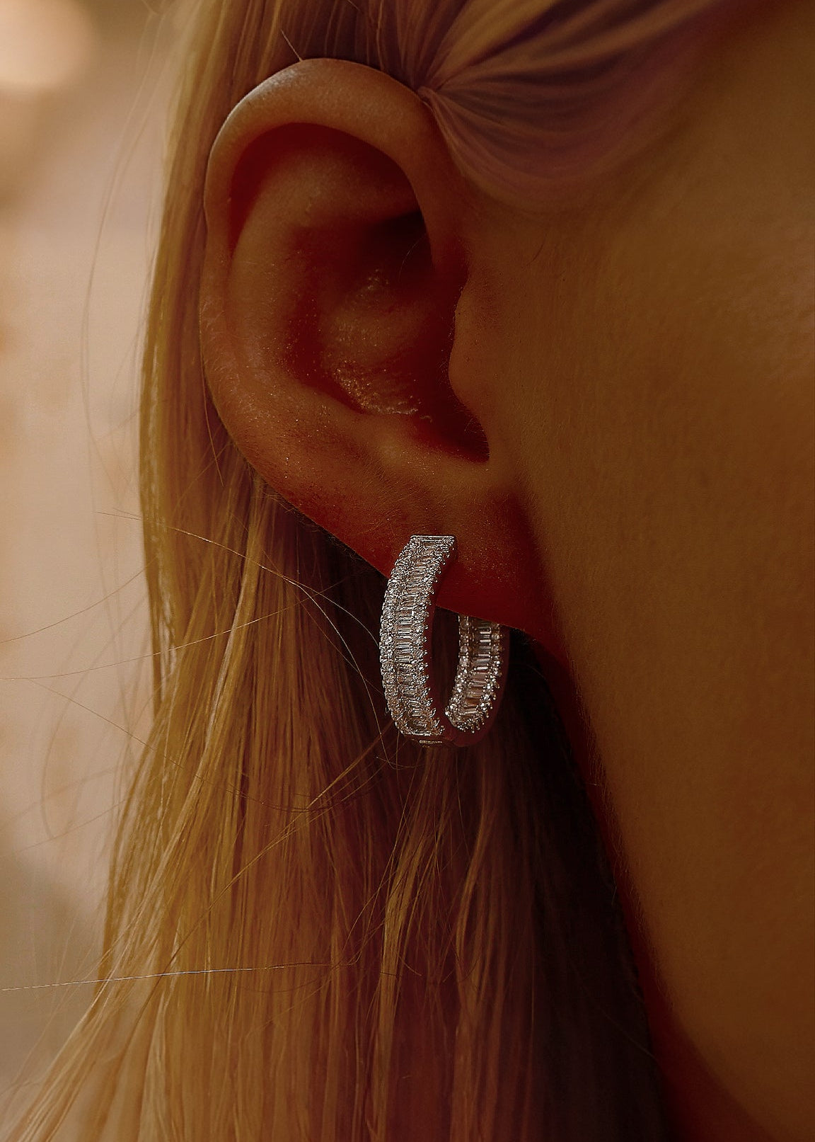 Close-up of an ear wearing a silver cubic zirconia hoop earring with blurred backgrounD