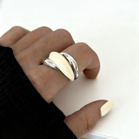 Hand wearing a silver cream ring on a white surface