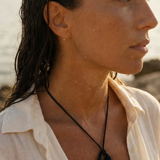 Woman wearing a black cord necklace and standing on a rocky coastline with ocean view